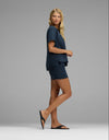 A woman stands sideways in front of a plain gray background, wearing the Cozy Earth Women’s Chelsea Short Sleeve Set in navy blue with black sandals. She has long blonde hair.|Color:Eclipse