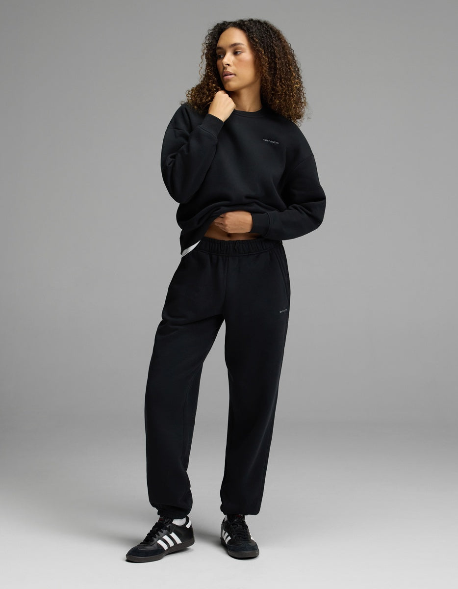 A person with curly hair wears the Women’s CityScape Crewneck & Sweatpant Set by Cozy Earth, standing in a relaxed pose against a plain gray background.
