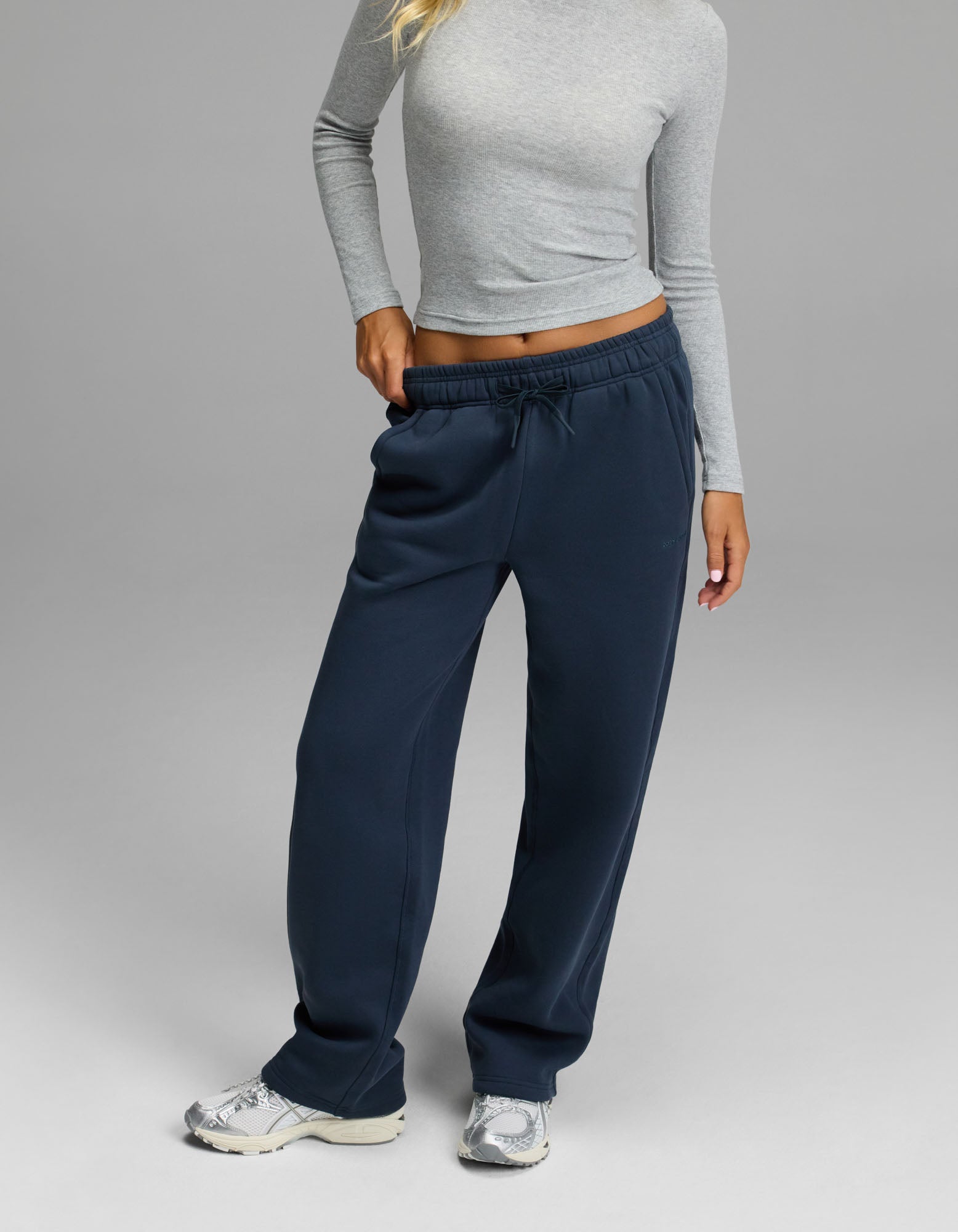 A person wearing a fitted gray long-sleeve top, Cozy Earth’s Women’s Cityscape Wide Leg Pant in Eclipse, and white sneakers stands against a plain gray background.|Color:Eclipse