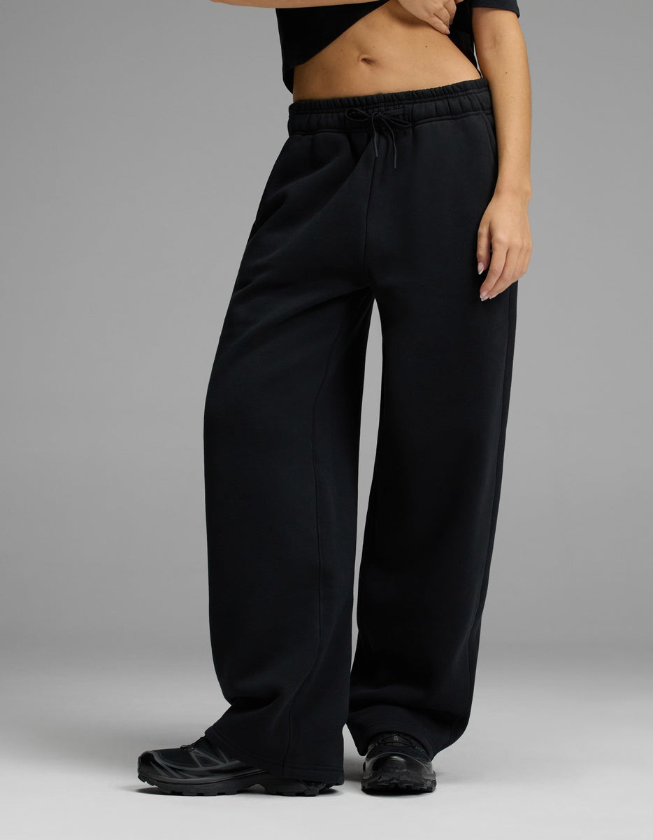 A person wearing the Cozy Earth Women’s CityScape Wide Leg Pant in Jet Black stands against a plain gray background, paired with a black cropped top and black sneakers. Their midriff and one hand are visible.|Color:Jet Black