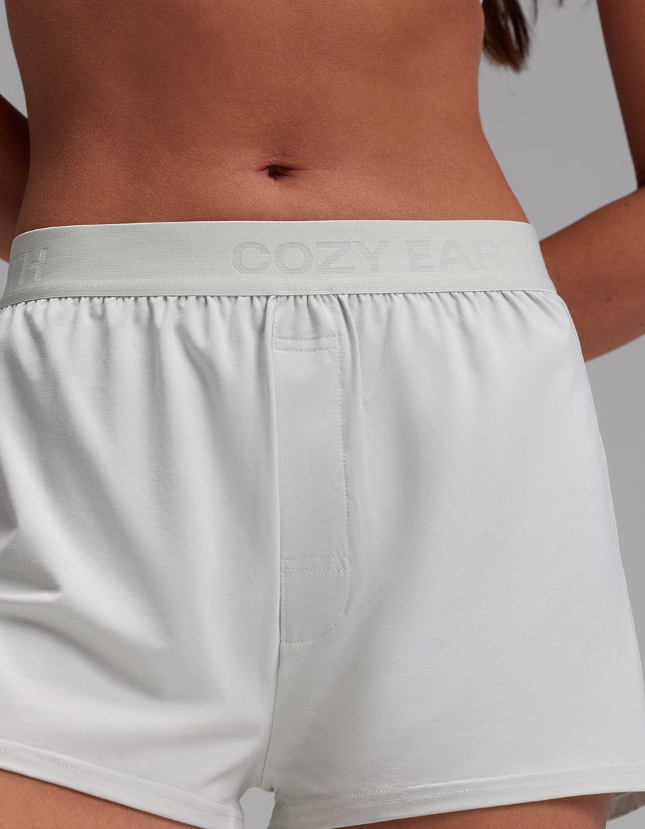 A person is shown from mid-torso to upper thighs against a plain background, wearing the Cozy Earth Women’s First Layer Pajama Boxer Short in white, featuring a high-waisted fit and elastic waistband.