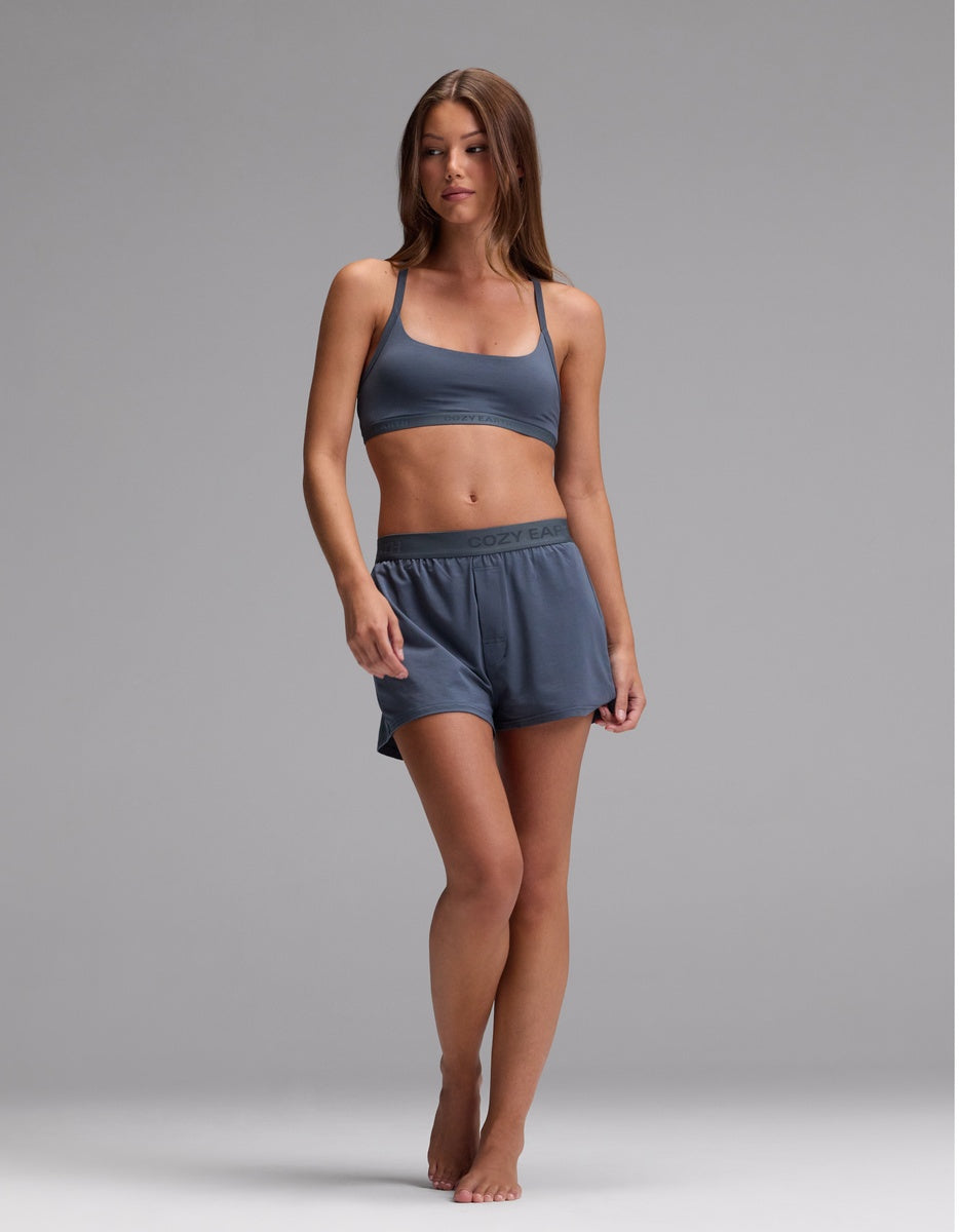 A woman stands barefoot against a plain background, wearing the Cozy Earth Women’s First Layer Pajama Soft Bra & Boxer Short Set in Dawn. She has long brown hair and a neutral expression.|Color:Dawn