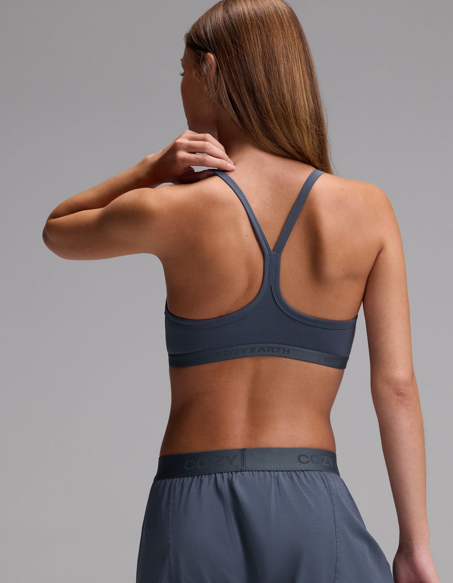 A woman with long brown hair is shown from the back, wearing the Cozy Earth Women’s First Layer Soft Bra in gray with matching shorts against a plain background.