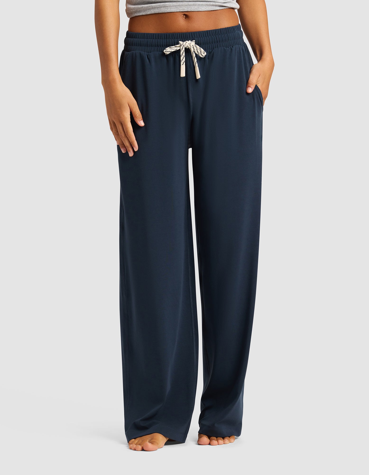 A person models the Cozy Earth Women's Studio Wide Leg Pant in navy, featuring white drawstrings. Only the lower torso and legs are visible, and they're standing barefoot against a plain light background.|Color:Eclipse