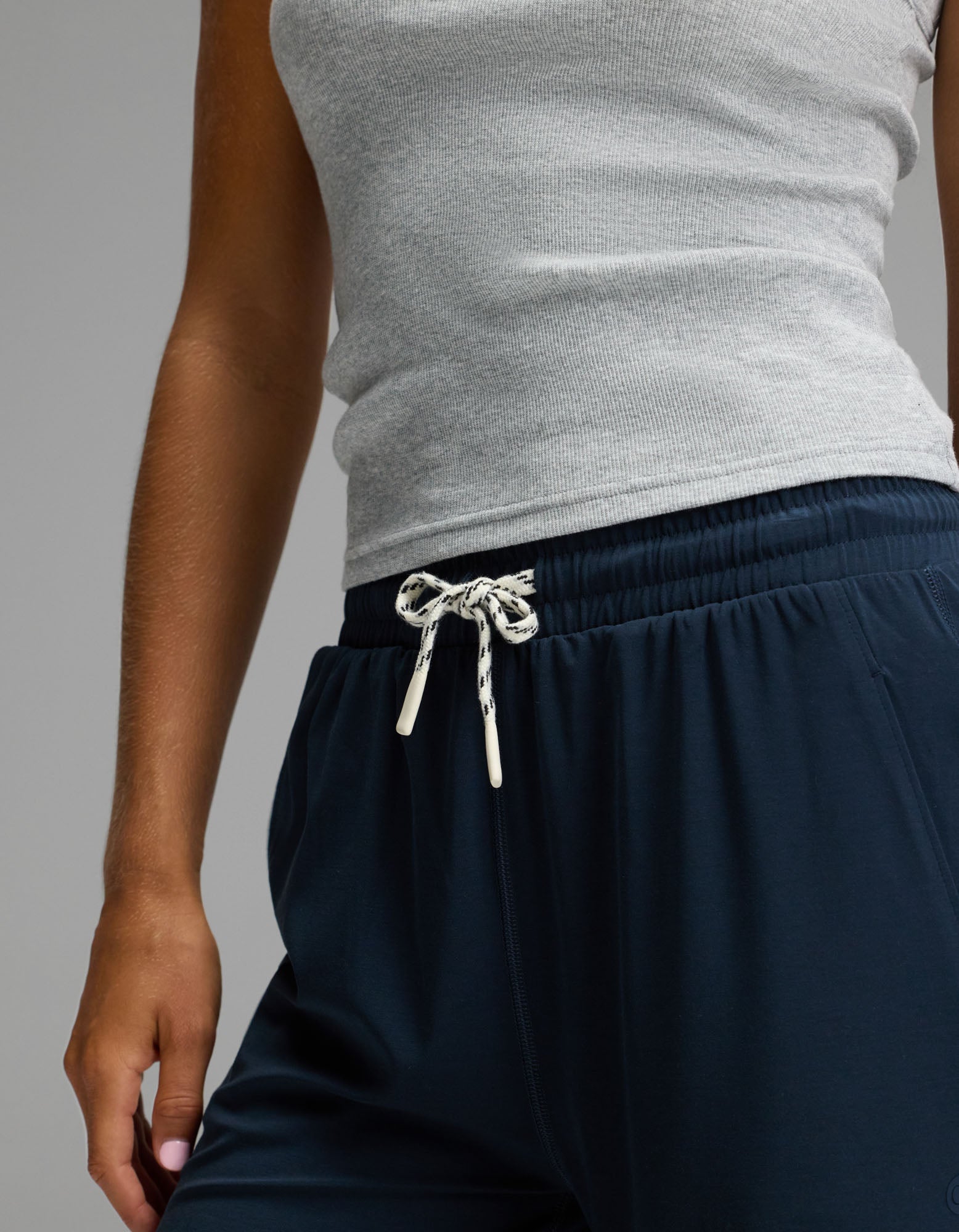 A person is shown from shoulder to mid-thigh wearing a gray ribbed tank top paired with Cozy Earth Women’s Studio Wide Leg Pant in navy blue, featuring a drawstring waist and one arm visible at their side.