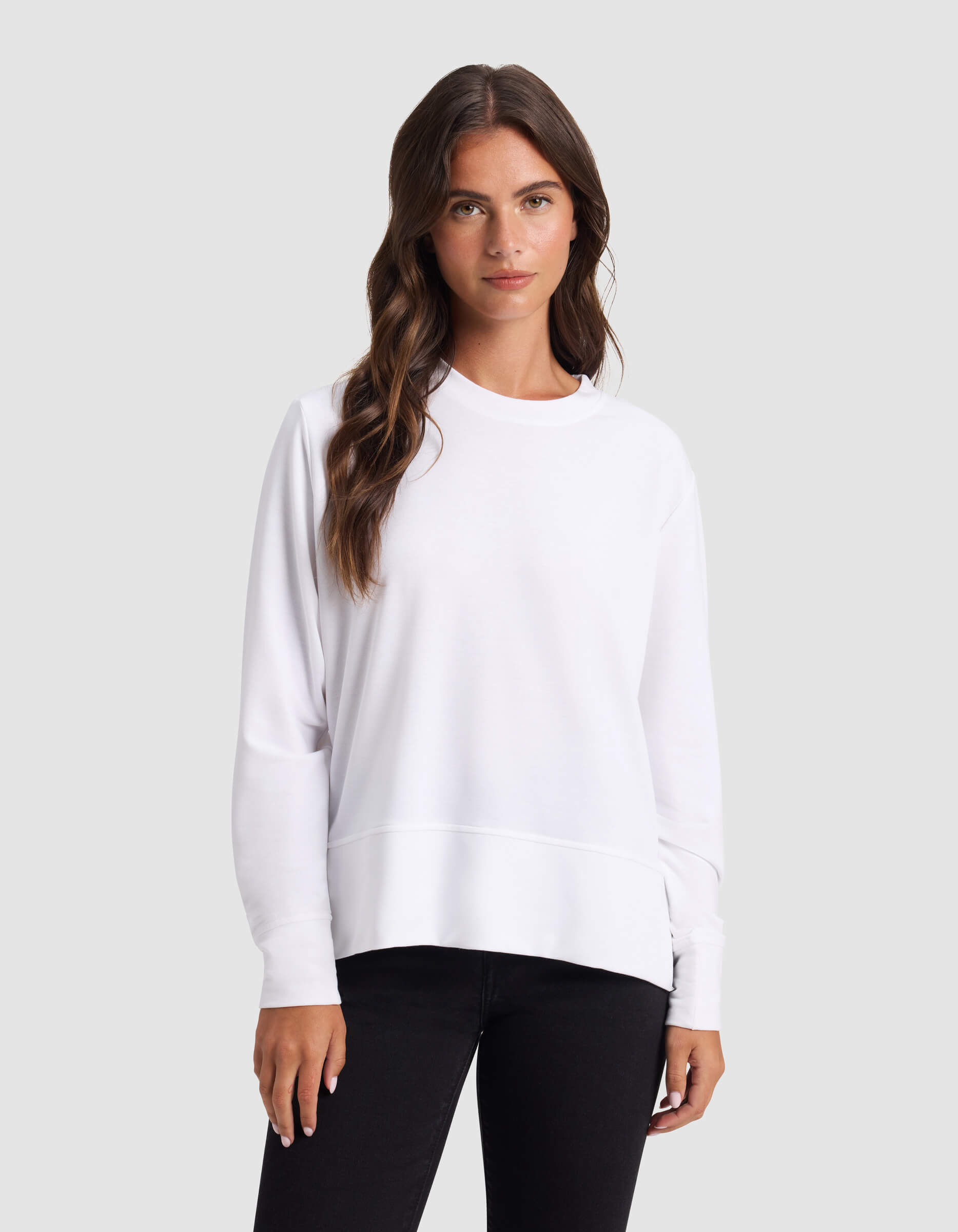 A woman with long brown hair models the Cozy Earth Women's StudioLite Crewneck, standing against a plain light gray background.|Color:White