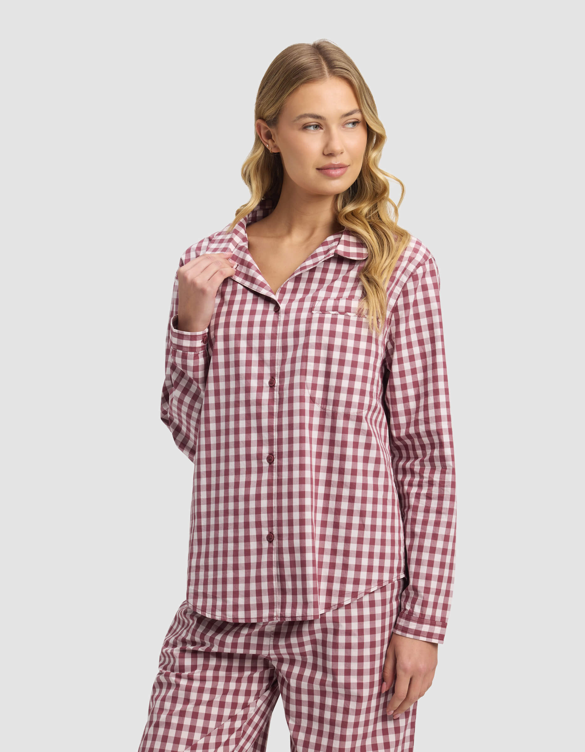 A woman with long blonde hair models the Cozy Earth Women's Sutton Long Sleeve Pajama Top, pink and white plaid, looking relaxed to the side against a light gray background.|Color:Mulberry Gingham