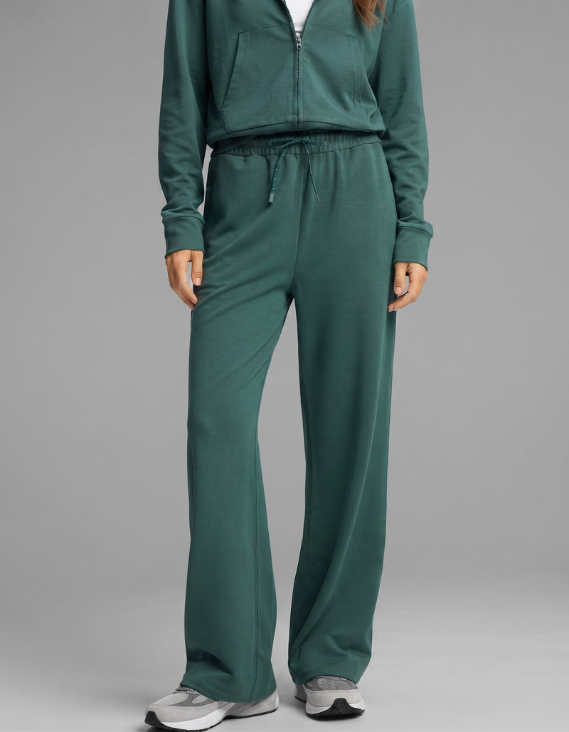 A person wearing the Cozy Earth Women's Versa Zip-Down Hoodie & Straight Leg Pant Set in green with gray sneakers, standing against a neutral background. The person’s face is not visible.