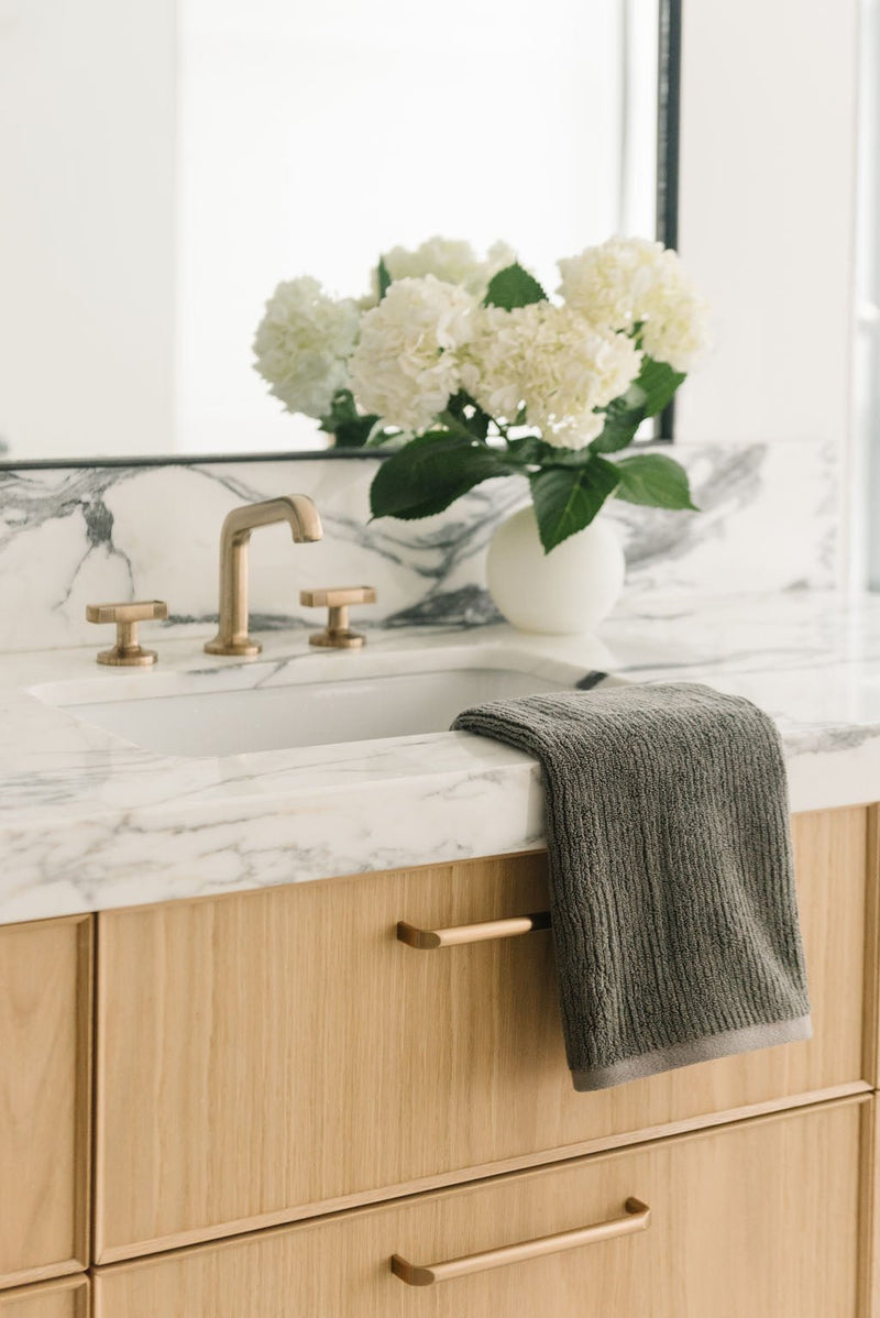 Ribbed Terry Hand Towels in the color charcoal. Photo of product taken with the product draped over a white marble sink.