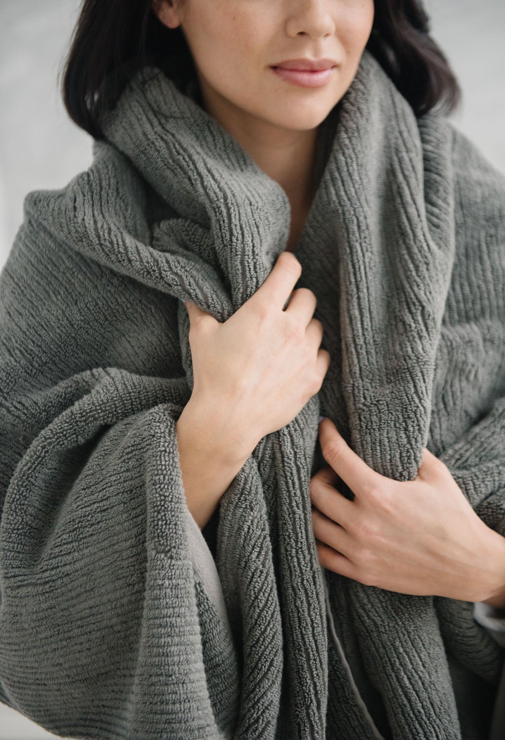 Ribbed Terry Bath Sheet in the color Charcoal. Photo of Ribbed Terry Bath Sheet taken with a woman who is wrapped in the Ribbed Terry Bath Sheet. 