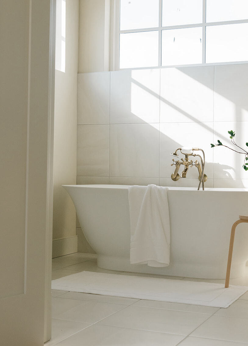 Premium Plush Bath Towel in the color white. The towel is draped over a bathtub. The bathroom that the bathtub is in is white. 